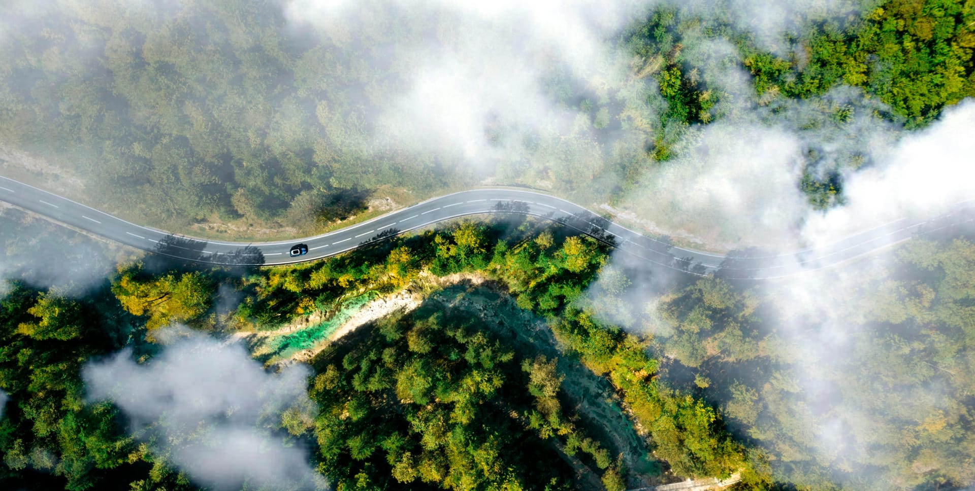 Scenic aerial view of a car driving through misty forested mountains, symbolizing Solavita's clean energy mission and commitment to sustainable and eco-friendly solutions